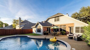 Un jardin avec une piscine, une terrasse dotée de mobilier d’extérieur et une maison en briques.
