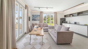 A modern living room with a sofa, a coffee table, and a kitchen area with cabinets and a microwave. - Thrilling Andros Villa | Villa Merope | 2 Bedrooms | Private Outdoor Pool |. (Andros)