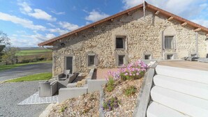 A stone building with a sloped roof, a small porch, and a paved entrance area with steps. - Gîte de charme à la campagne Charroux (Charroux)