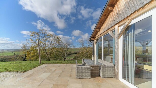 A patio with stone flooring, wicker furniture, and a glass door leading to a view of a countryside landscape. - Gîte de charme à la campagne Charroux (Charroux)