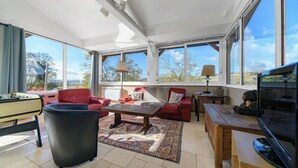 A spacious living room with a red sofa, a coffee table, and a television. Large windows provide natural light and views of the outdoors. - Gîte de charme à la campagne Charroux (Charroux)