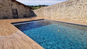 A rectangular swimming pool with clear blue water, surrounded by a stone wall and wooden deck. - Gîte de charme à la campagne Charroux (Charroux)