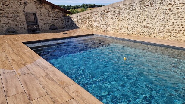 A rectangular swimming pool with clear blue water, surrounded by a stone wall and wooden deck. - Gîte de caractère Charroux La Samandre (Charroux)