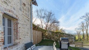 A stone building with a patio area featuring a table and chairs, a barbecue grill, and a view of the surrounding landscape. - Gîte de caractère Charroux La Samandre (Charroux)