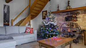 A cozy living room with a wooden staircase, a decorated Christmas tree, a white sofa, and a wooden coffee table. - Gîte de caractère Charroux La Samandre (Charroux)