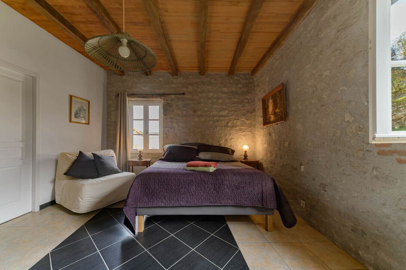 A bedroom with a bed, a chair, a window, and a wooden ceiling.