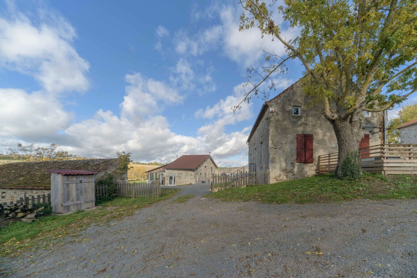 A rural property with a stone barn, a wooden fence, and a gravel driveway.