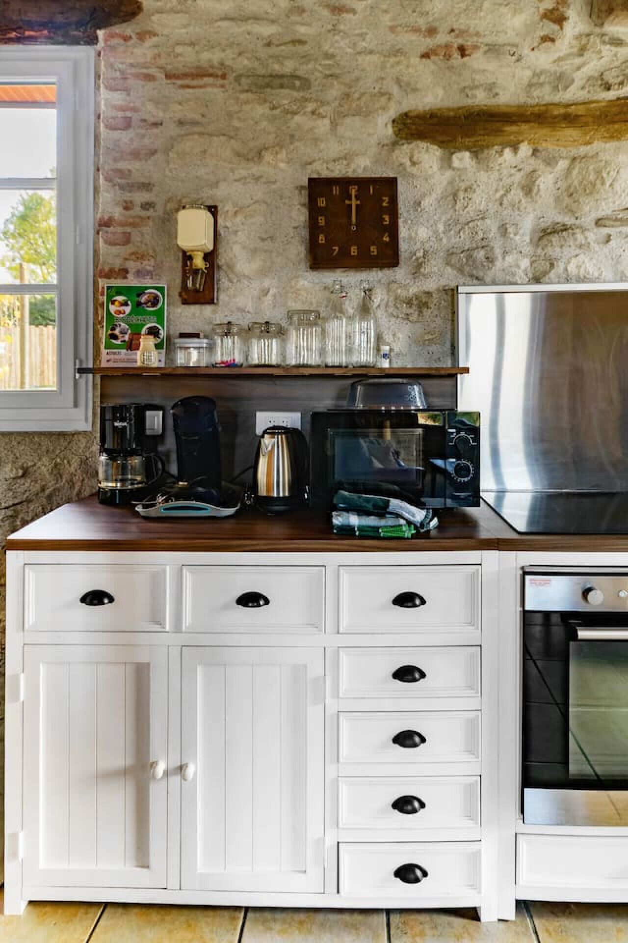 A kitchen with white cabinetry, a stainless steel refrigerator, a coffee maker, a microwave, and a clock on the wall.