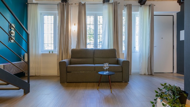 En stue med en sofa, et lille bord med glas, en trappe og en dør.