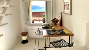 Uma cozinha compacta com vista para o mar, uma mesa de jantar com cadeiras e uma pequena planta em vaso.