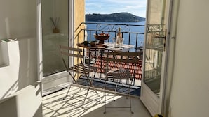 Varanda com mesa posta para refeições, com vista para um corpo d'água e uma colina distante.
