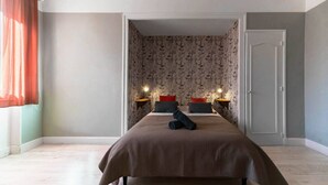 Ein Schlafzimmer mit einem großen Bett, zwei Nachttischen mit Lampen, einer Tür und einem mit Vorhängen versehenen Fenster.