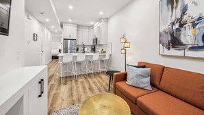 A modern kitchen with white cabinets, a stainless steel refrigerator, and a bar area with white chairs.