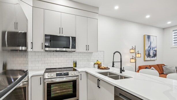 A modern kitchen with stainless steel appliances, white cabinetry, and a central island with a sink.
