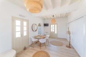 Une pièce lumineuse et blanche, avec une table de salle à manger ronde, des chaises blanches et des tapis tissés.