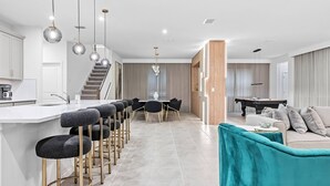 Una cocina moderna con barra, zona de comedor y sala de estar con sofá y mesa de billar.