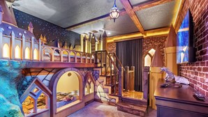 Una habitación infantil con una casita temática de castillo, una escalera y una cama.