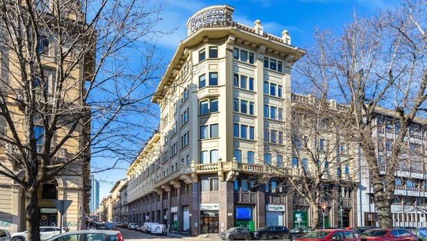 Ein mehrstöckiges Hotel im klassischen Stil, mit einem markanten Hauseingang an der Ecke und mehreren Geschäften im Erdgeschoss.