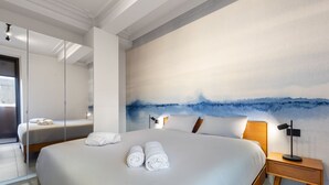 Ein modernes Hotelzimmer mit einem großen Bett, einem Nachttisch mit Lampe und einem großen abstrakten Gemälde an der Wand.