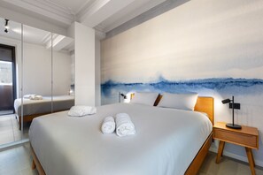 Ein modernes Hotelzimmer mit einem großen Bett, einem Nachttisch mit Lampe und einem großen abstrakten Gemälde an der Wand.