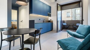 Eine moderne Küche mit blauen Schränken, ein Essbereich mit rundem Tisch und Stühlen sowie eine Sitzecke mit einem blauen Sofa.
