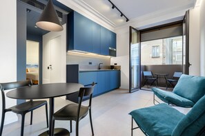 Eine moderne Küche mit blauen Schränken, ein Essbereich mit rundem Tisch und Stühlen sowie eine Sitzecke mit einem blauen Sofa.