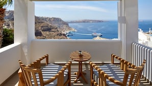 A balcony with a table and chairs, overlooking a coastal landscape with cliffs and a ship in the distance. - Magnificent Santorini Villa | Villa Aphrodite’s Dream | 2 Bedrooms |. (Santorini)