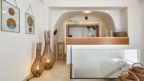 A modern interior with a glass partition, wooden reception desk, and decorative wall art. - Magnificent Santorini Villa | Villa Aphrodite’s Dream | 2 Bedrooms |. (Santorini)