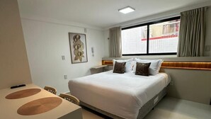 Een moderne hotelkamer met een groot bed, nachtkastje, stoel en raam met gordijnen.