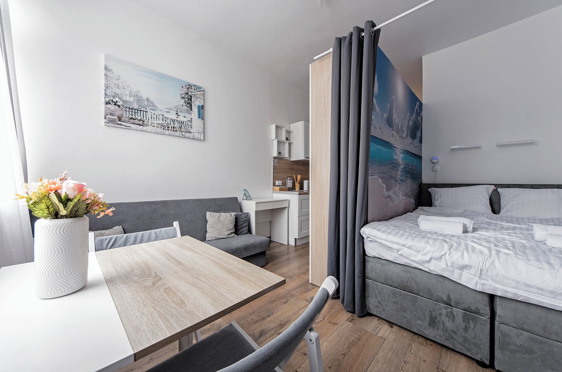A modern hotel room with a bed, a desk, and a small kitchenette.