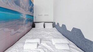 Een moderne hotelkamer met een groot bed, witte lakens en een muurschildering van een strand.