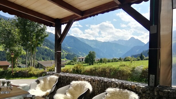 Ein überdachter Außenbereich mit Steinmauern, weißen, flauschigen Stühlen und Blick auf die Berge.