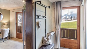 Ein Zimmer mit einer hölzernen Sitzbank, einem Wandregal, einem Heizkörper und Blick auf eine verschneite Landschaft durch ein großes Fenster.
