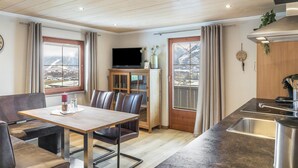 Eine moderne Küche mit Einbauherd, ein Essbereich mit Tisch und Stühlen sowie ein Fernseher in der Ecke.