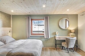 Un dormitorio con cama, escritorio, silla, espejo y ventana con cortinas.