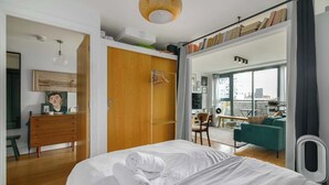 A bedroom with a bed, a wooden wardrobe, a desk, and a view of the city through large windows. - Charming Central Studio with Balcony in Birmingham (West Midlands)