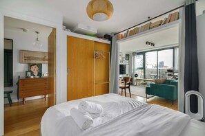 A bedroom with a bed, a wooden wardrobe, a desk, and a view of the city through large windows. - Charming Central Studio with Balcony in Birmingham (West Midlands)