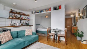 A compact living space with a kitchenette, a sofa, a dining area, and a bedroom. - Charming Central Studio with Balcony in Birmingham (West Midlands)