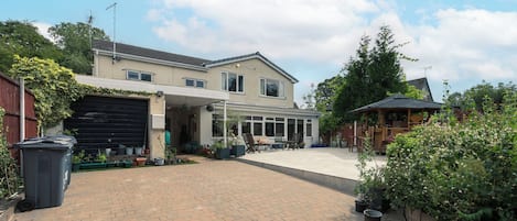 A two-story house with a covered driveway, outdoor seating area, and a garden.