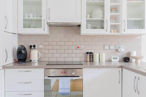 A modern kitchen with white cabinets, a built-in oven, and a coffee maker. - Tastefully Curated 2BD Flat in Maida Vale, London (Greater London)
