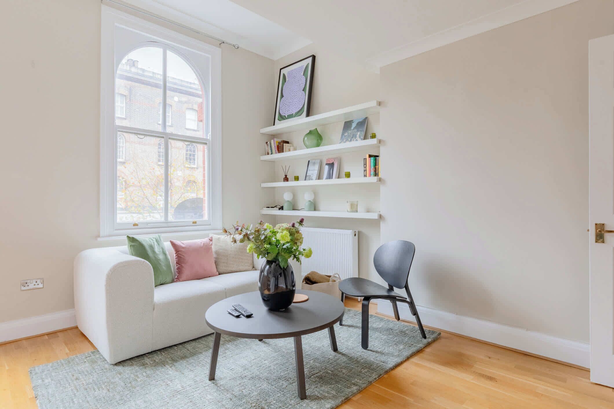 A modern living room with a white sofa, a round coffee table, a grey armchair, a bookshelf, and a large window.