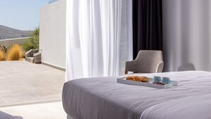 Een moderne hotelkamer met een groot bed, een dienblad met gebak en drankjes, en uitzicht op het omliggende landschap.