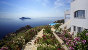 A coastal property with a stone pathway, lush garden, and a view of the sea and a distant island.