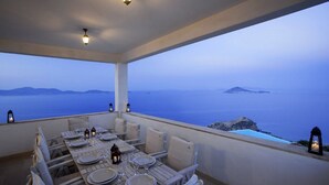 A dining area with a table set for four, overlooking a scenic view of the sea and distant islands.