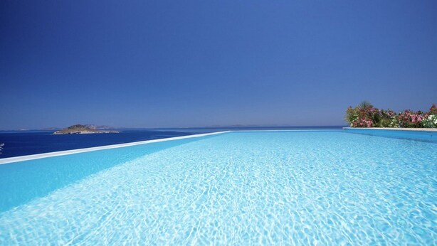 A clear blue infinity pool with a view of the ocean and a small island.