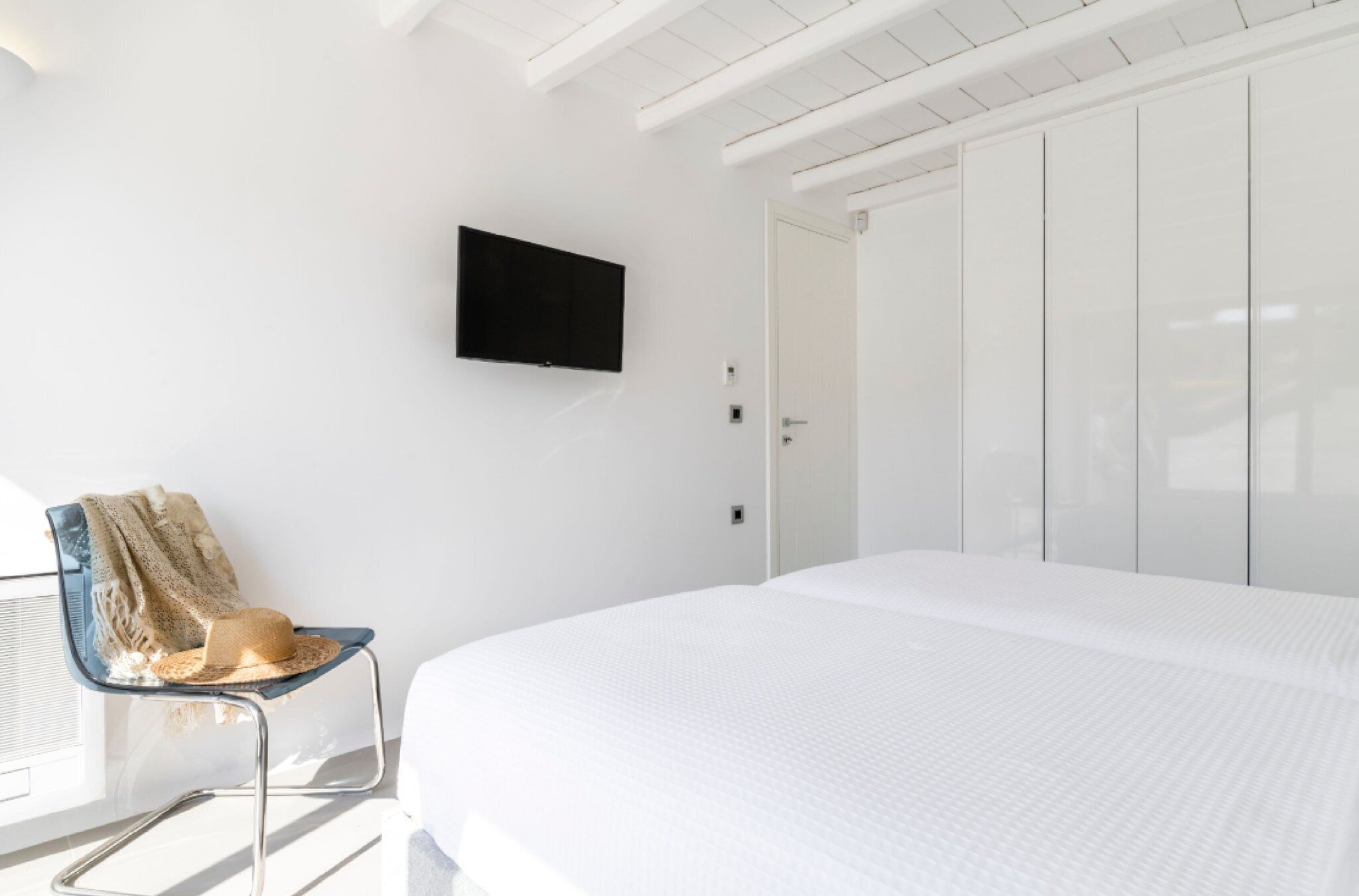 Een slaapkamer met een bed, een aan de muur bevestigde televisie, een stoel met een plaid en een kledingkast.