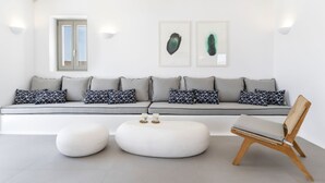 Un salon moderne avec un canapé gris, des coussins à motifs, un pouf rond blanc et une chaise en bois.