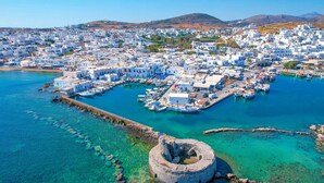 A coastal town with white buildings, a harbor with boats, and a historic fort. - Endearing Santorini Villa | Villa Delphi | 2 Bedrooms | Breathtaking Caldera. (Santorini)
