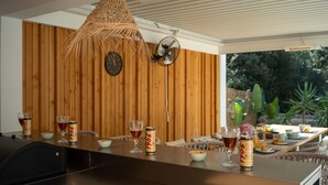 A dining area with a wooden wall, a clock, and a table set with drinks and snacks. - Villa 'Marloria' with Mountain Views, Wi-Fi, and Air Conditioning (Crestatx)