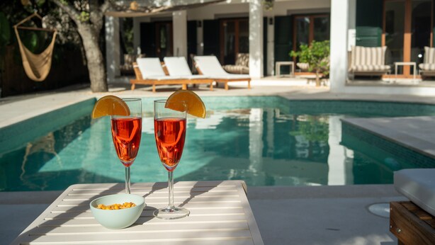 A poolside setting with two glasses of red drink, a bowl of snacks, and lounge chairs in the background. - Villa 'Marloria' with Mountain Views, Wi-Fi, and Air Conditioning (Crestatx)